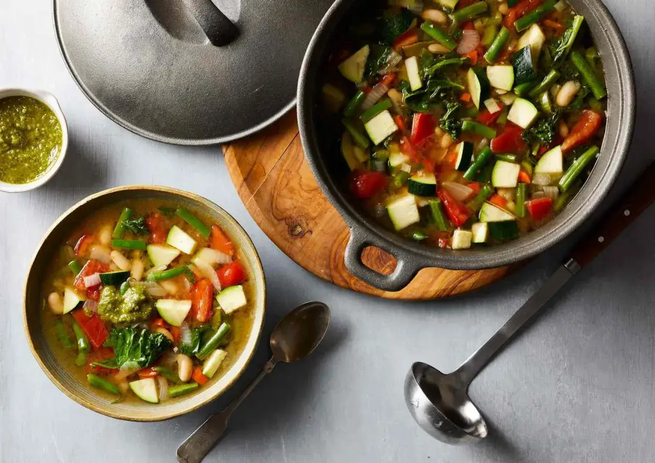 En sk&aring;l med nyttig soppa g&aring; ner i vikt, full av gr&ouml;nsaker som zucchini, b&ouml;nor och tomater. En gryta med samma soppa st&aring;r bredvid.