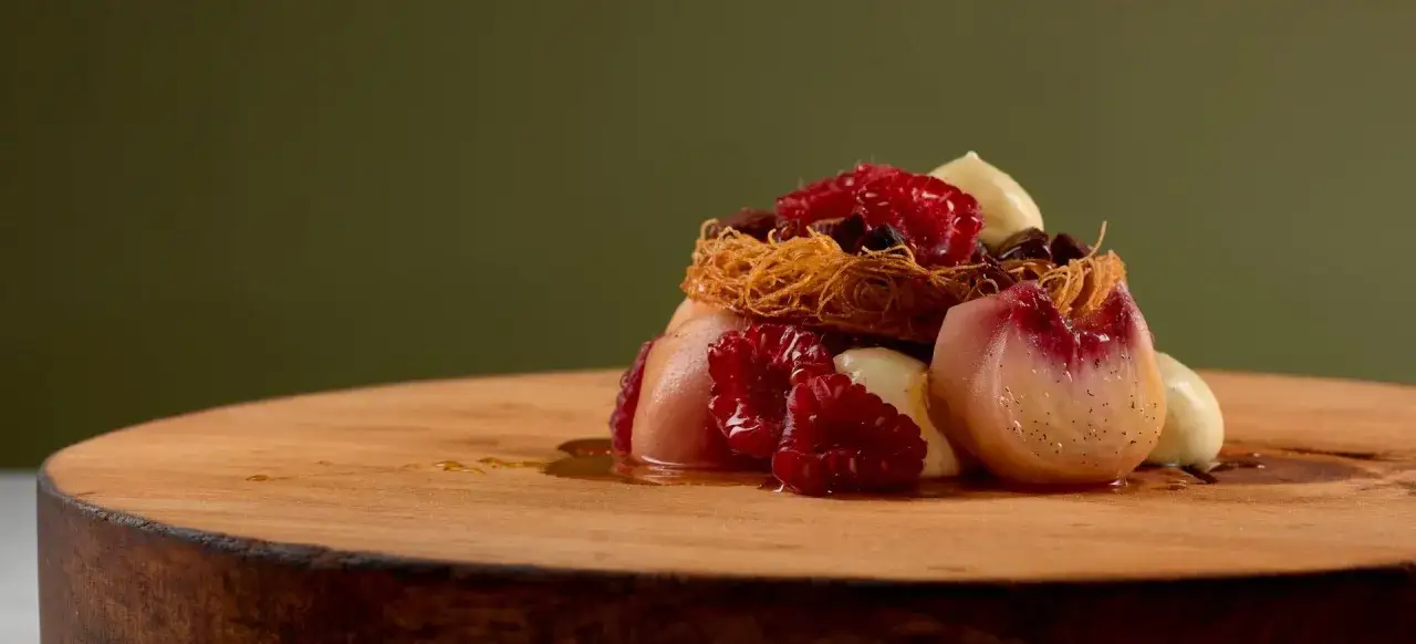 En elegant dessert med pocherad persika, hallon och vaniljkräm, en modern tolkning av peach melba.