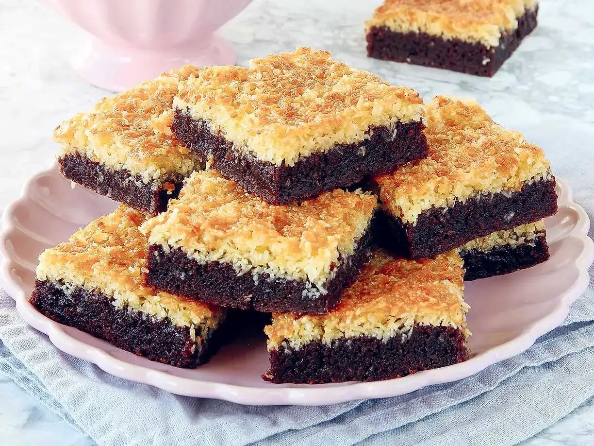 En långpanna med saftiga kokostosca-bitar, med en mörk chokladbotten och ett gyllene kokostäcke.