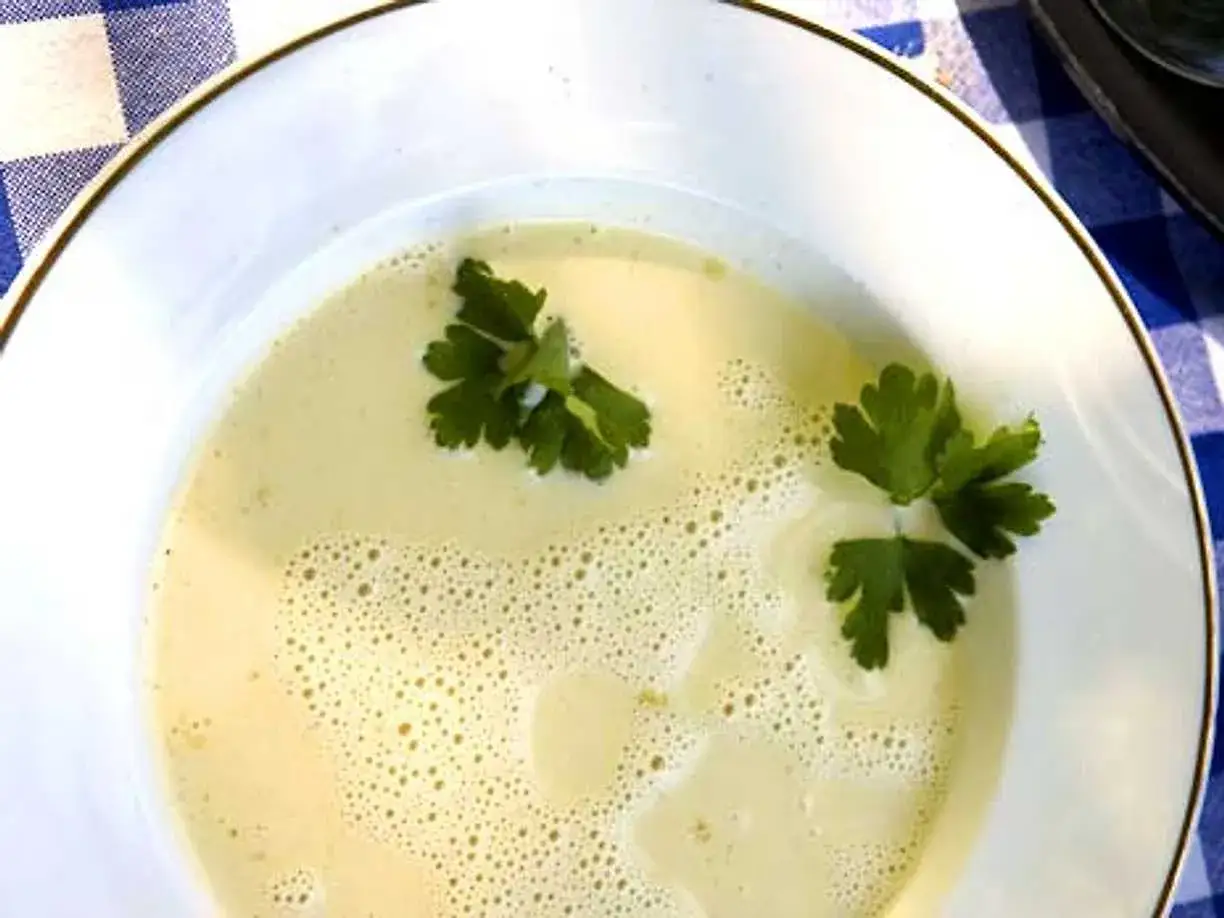 En krämig vit sparrissoppa med persilja, serverad i en vit skål med guldkant.