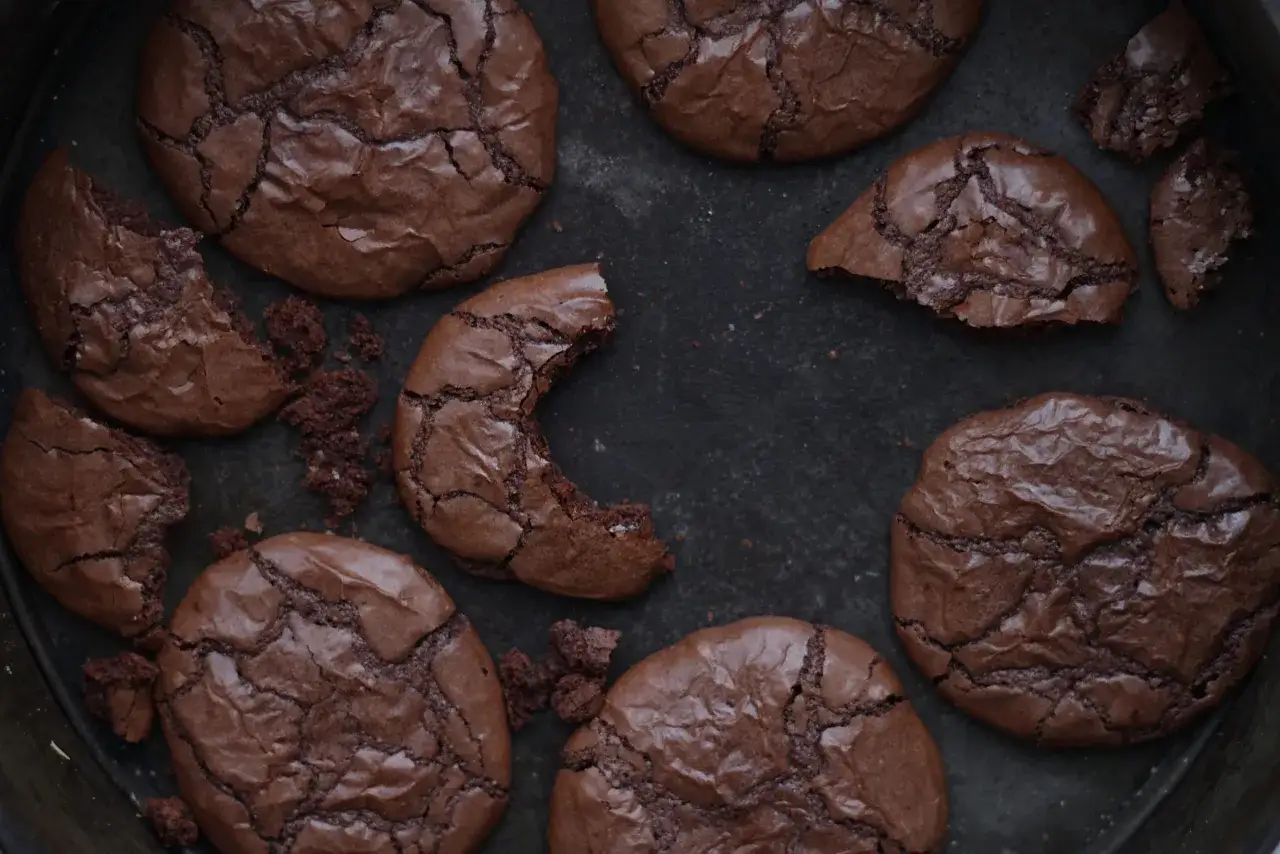 Mörka, spröda chokladkakor med synliga sprickor, perfekta att baka med Nutella. Några är hela, andra har bitar som saknas.