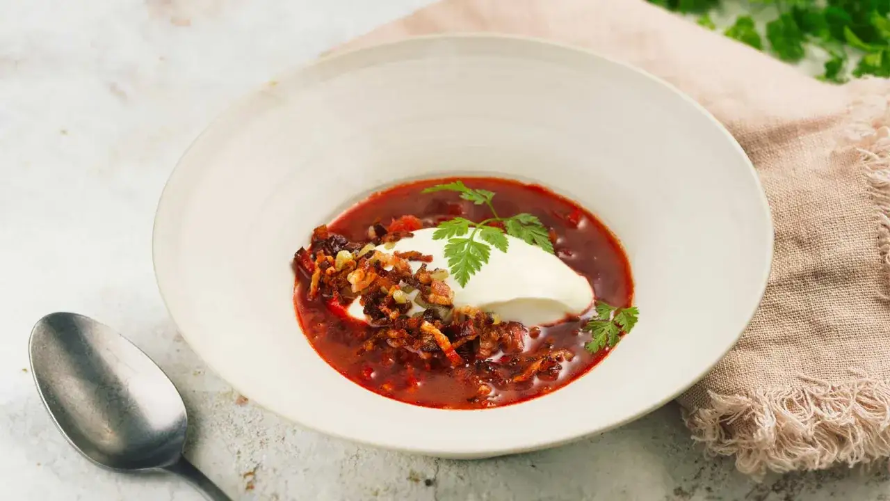 En skål med röd borsjtj, toppad med en klick gräddfil och krispiga bitar. Ett perfekt borsjtj recept för en kall dag.