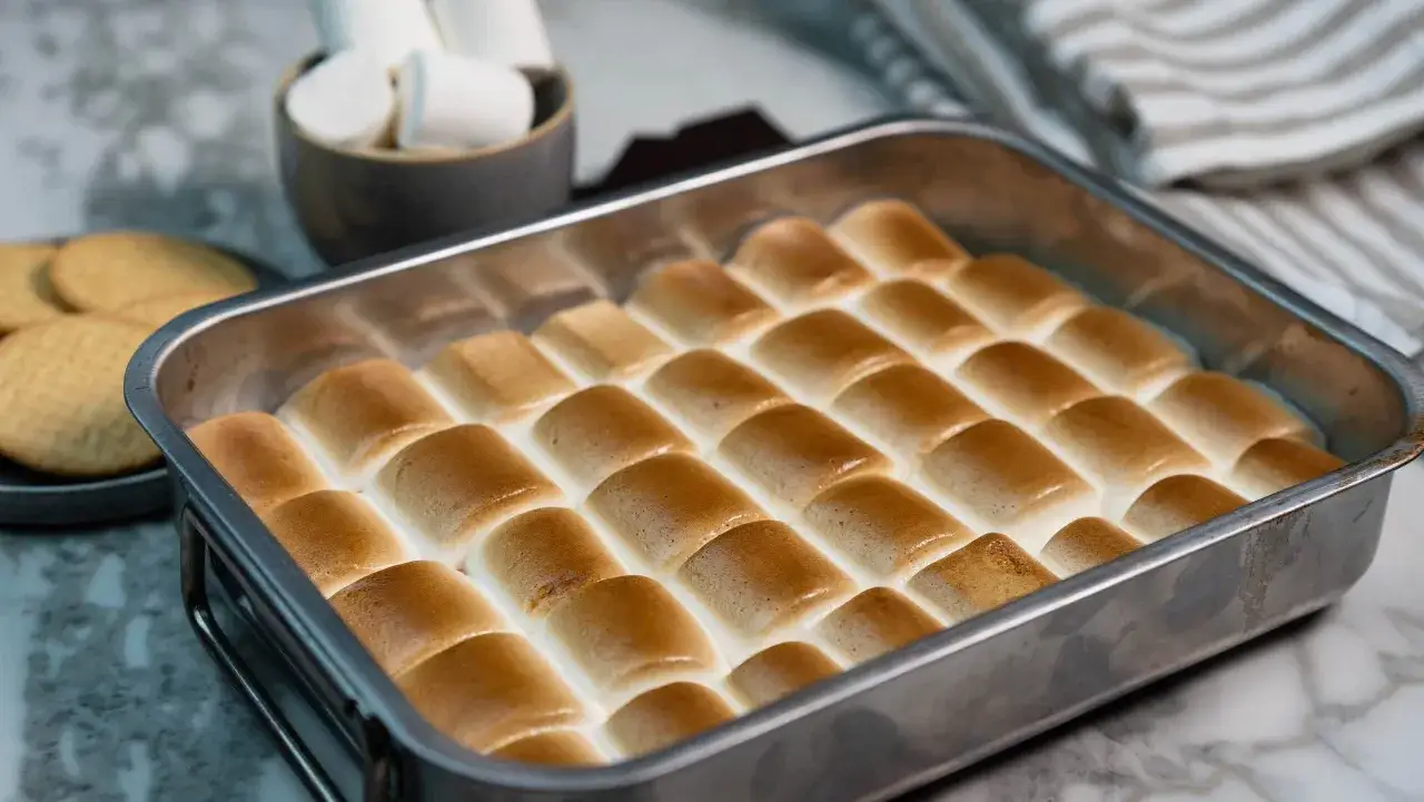 S'mores i ugn, gyllene marshmallows som smälter över choklad och kex i en ugnsform. En härlig dessert som väntar på att avnjutas.