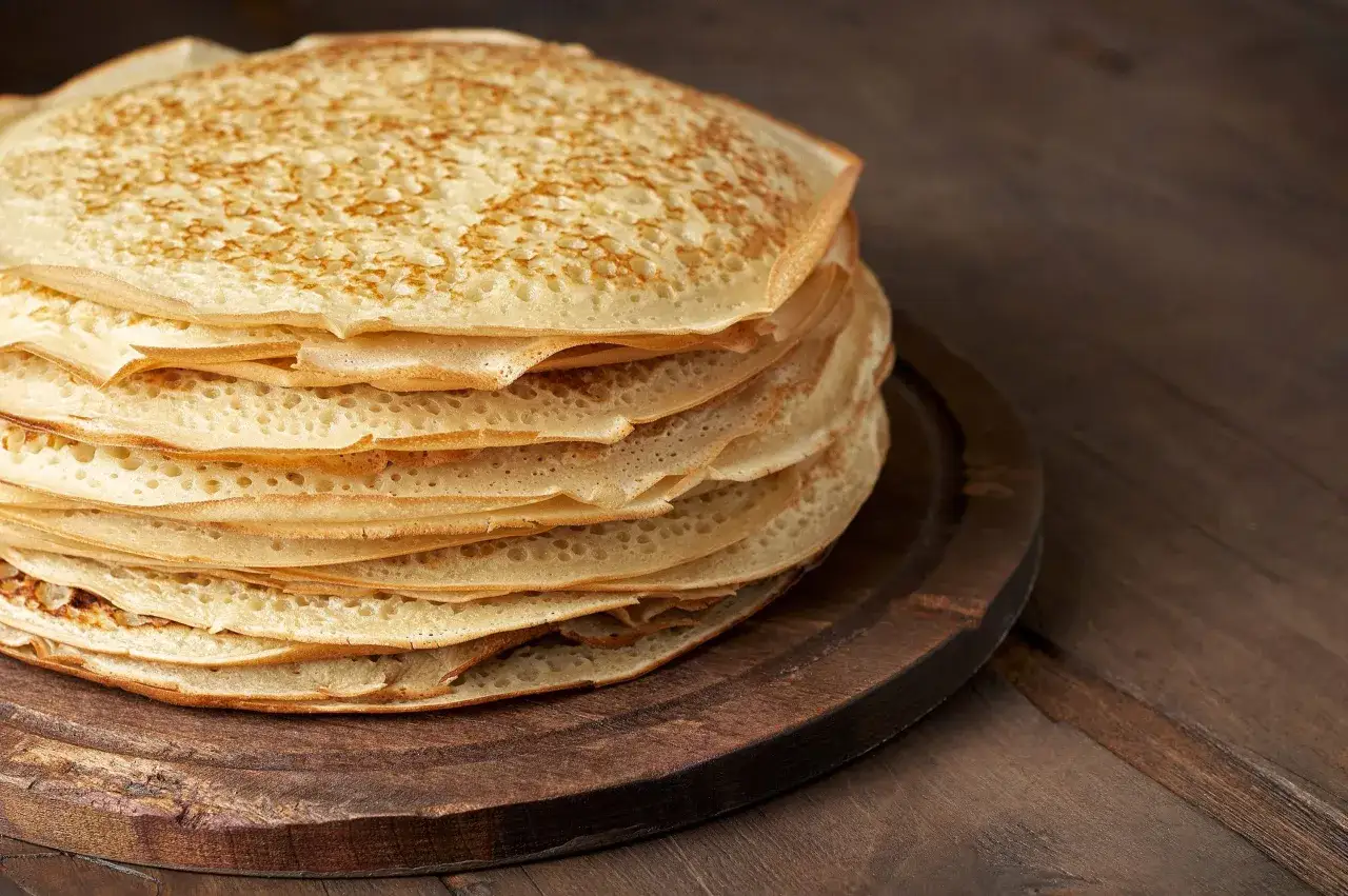 En hög med gyllene pannkakor på en träbricka. Perfekt för att frysa in och njuta av senare.