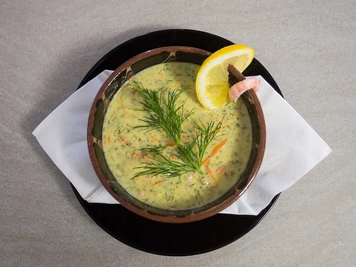 Krämig soppa med räkor, dill och morötter, garnerad med en citronskiva och en räka.