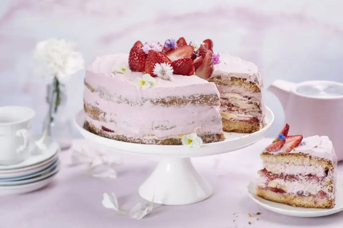 Enkel jordgubbstårta med rosa frosting, färska jordgubbar och små blommor. En bit är upplagd på en tallrik.