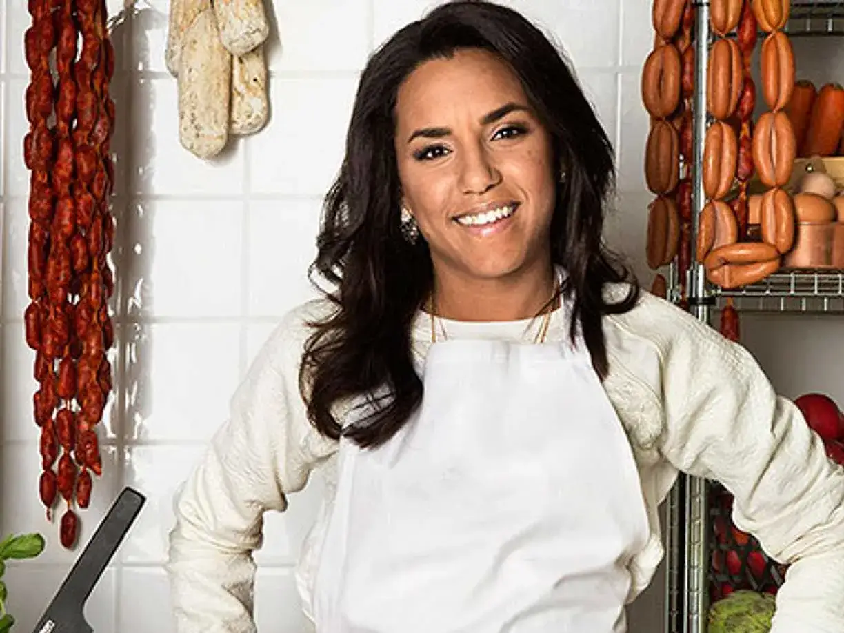 Markiz Tainton, en glad slaktare, ler i sitt kök omgiven av korvar och kött.