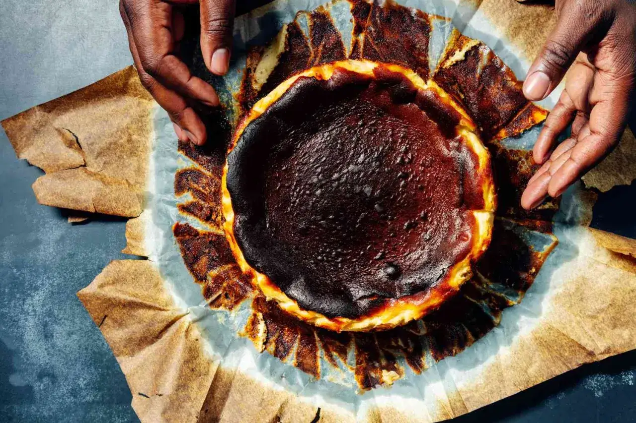 En mörk, karamelliserad baskisk cheesecake med brända kanter, varsamt lyft ur sitt bakplåtspapper.