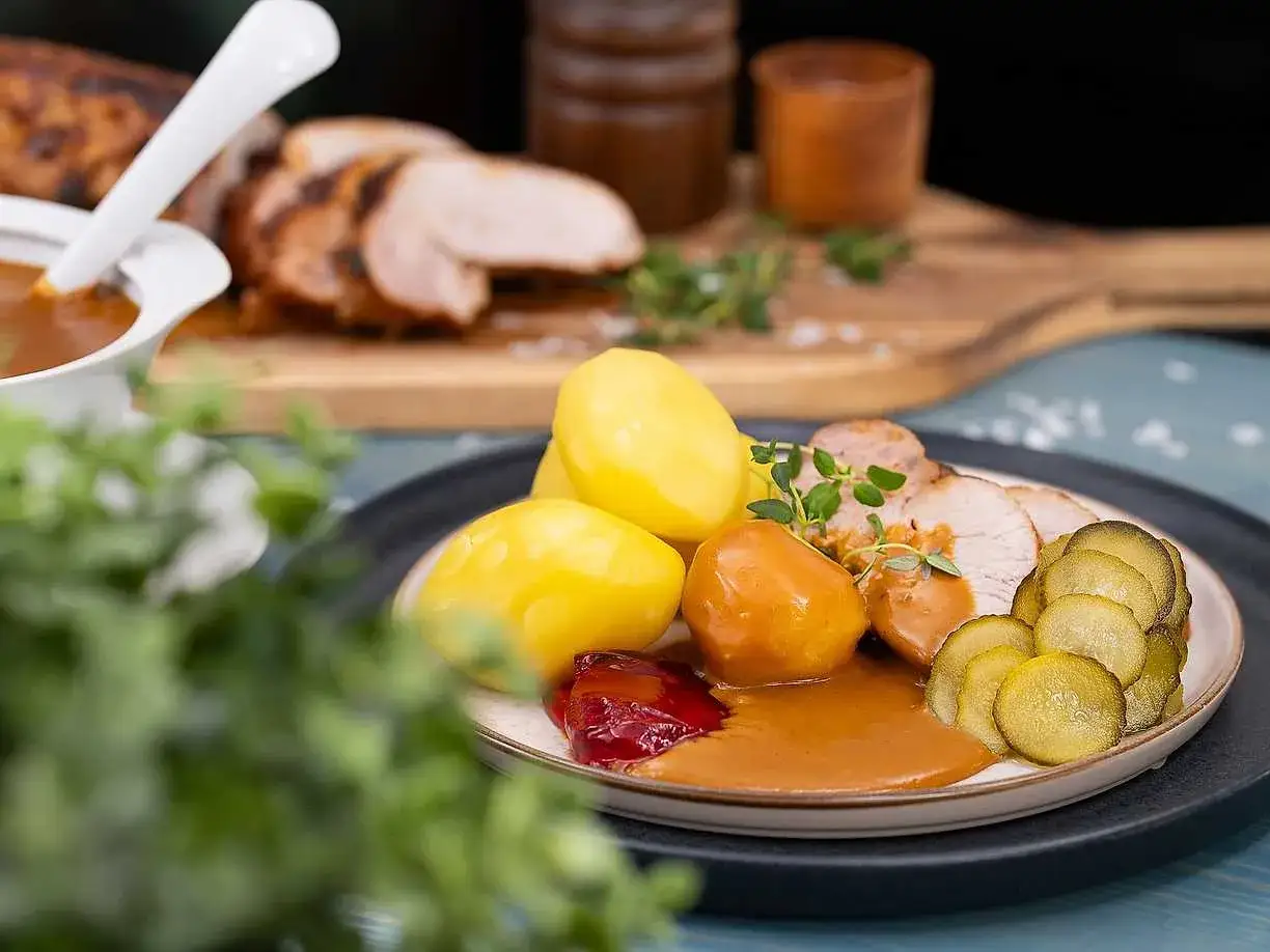 En tallrik med skivad ytterfile i sockerkaksform, potatis, lingonsylt och s&aring;s. Serveras med gurka och en kvist timjan.