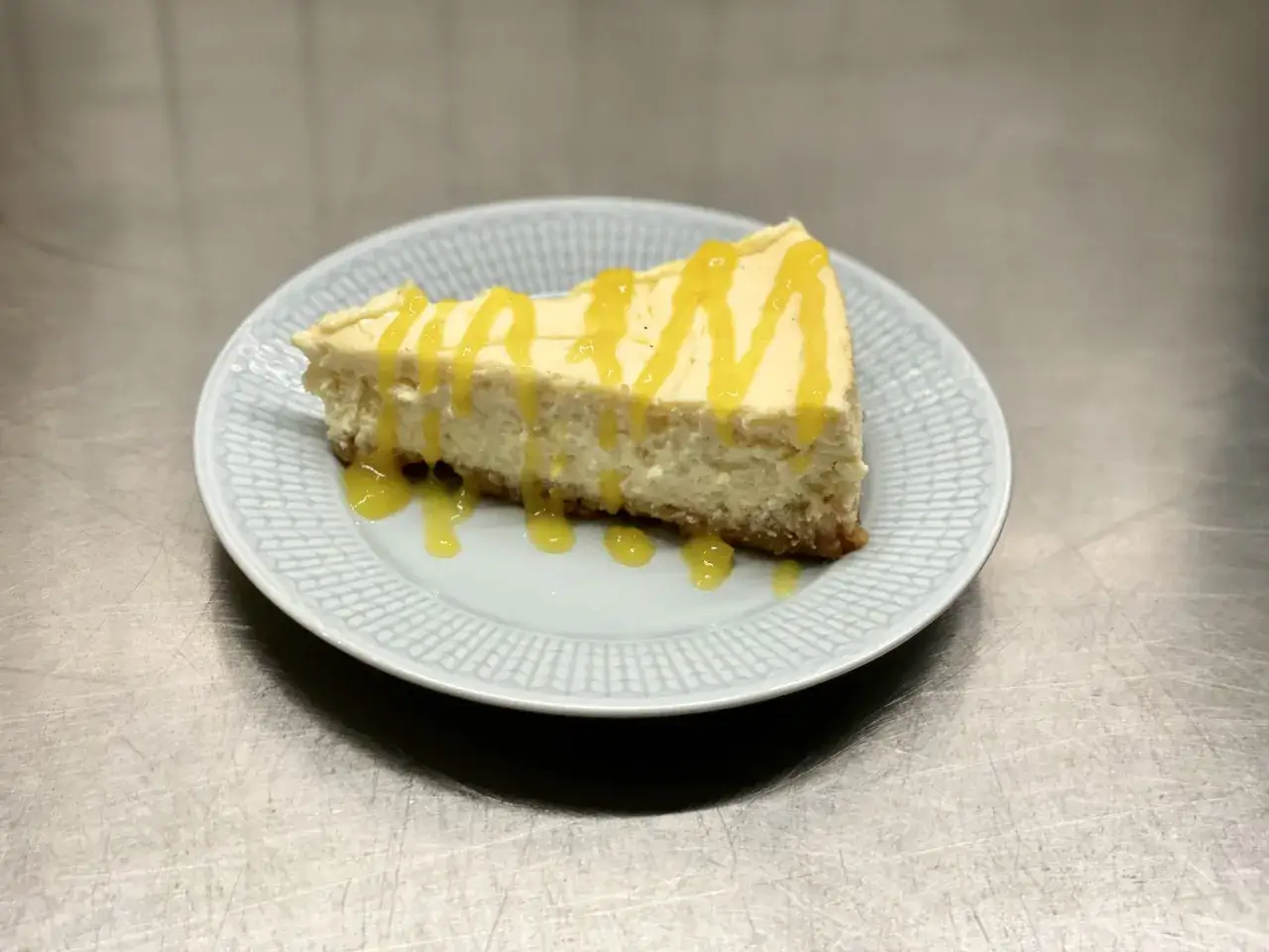 En bit krämig mango cheesecake med gul glasyr på en ljusblå tallrik.