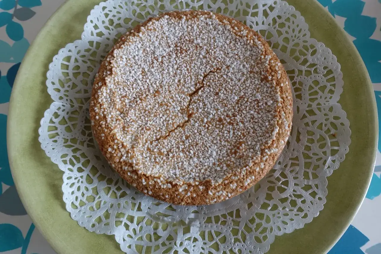 En gyllene sockerkaka med kardemumma, toppad med pärlsocker, ligger på en grön tallrik med en vacker spetsduk.