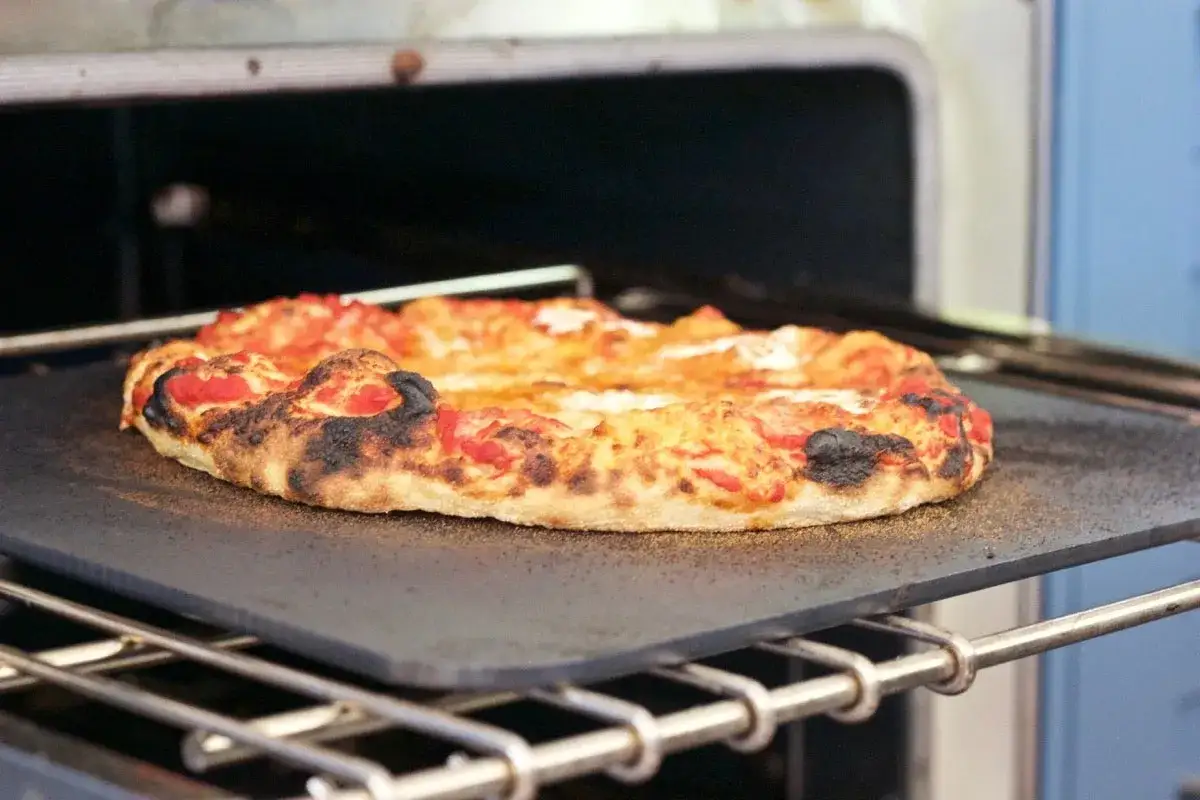 En pizza med bubblande ost och lite brända kanter på en pizzasten i ugnen. Pizzadegen ser perfekt krispig ut.