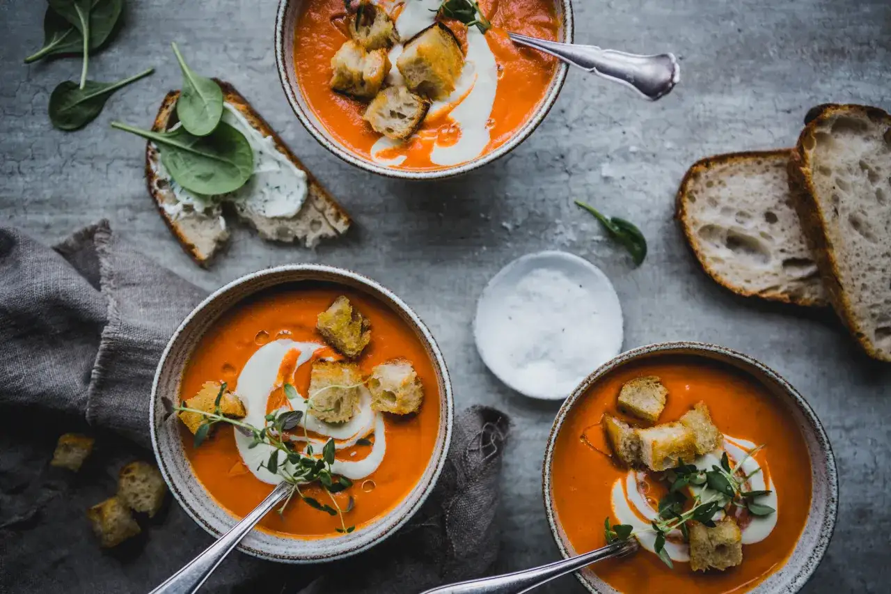 Tre skålar med krämig tomatsoppa, gjord på passerade tomater, toppas med krutonger och en virvel av grädde. Serveras med gott bröd och färsk spenat.