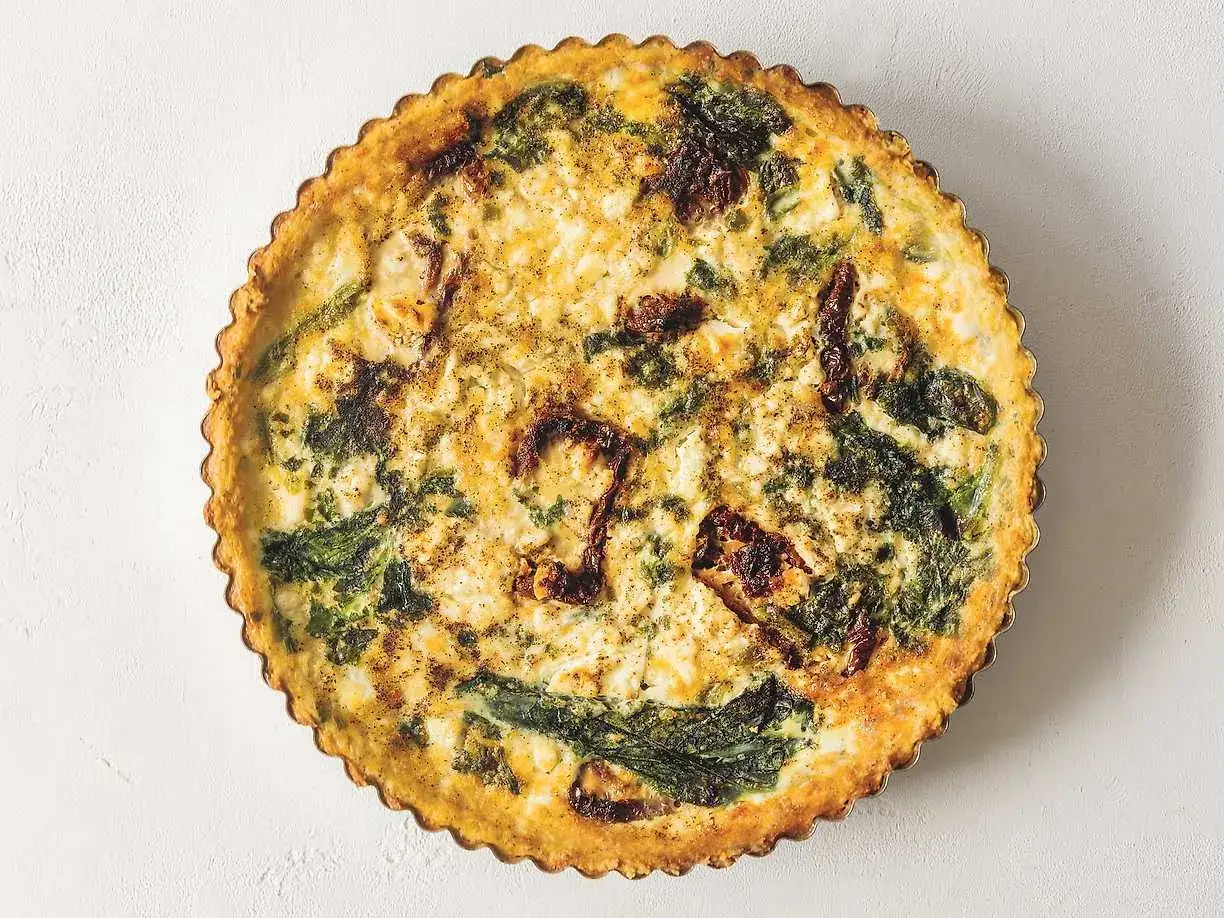 En gyllene, smakrik vegetarisk paj med gröna bladgrönsaker och soltorkade tomater i en krispig pajdeg.