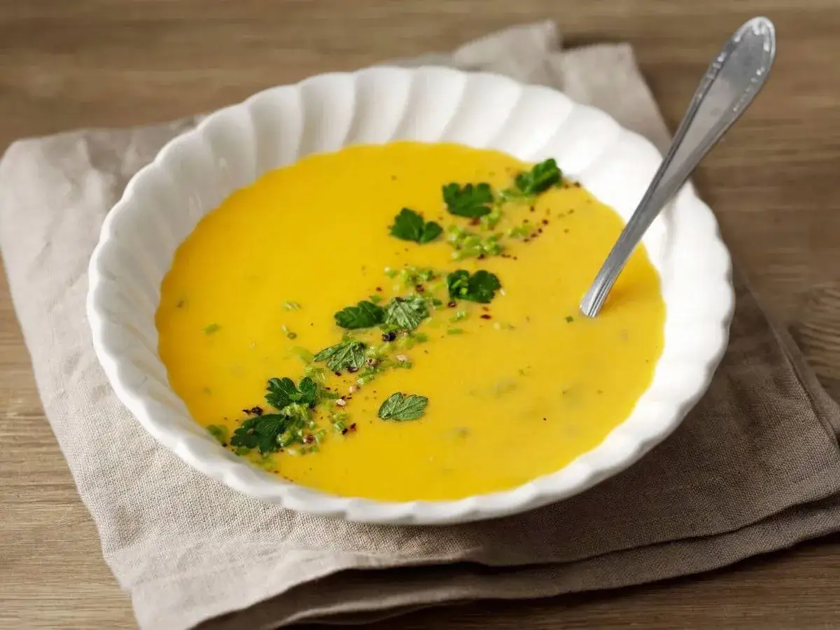 En krämig morotssoppa med en klick creme fraiche, garnerad med färska örter och peppar. Serveras i en vit skål med en sked.