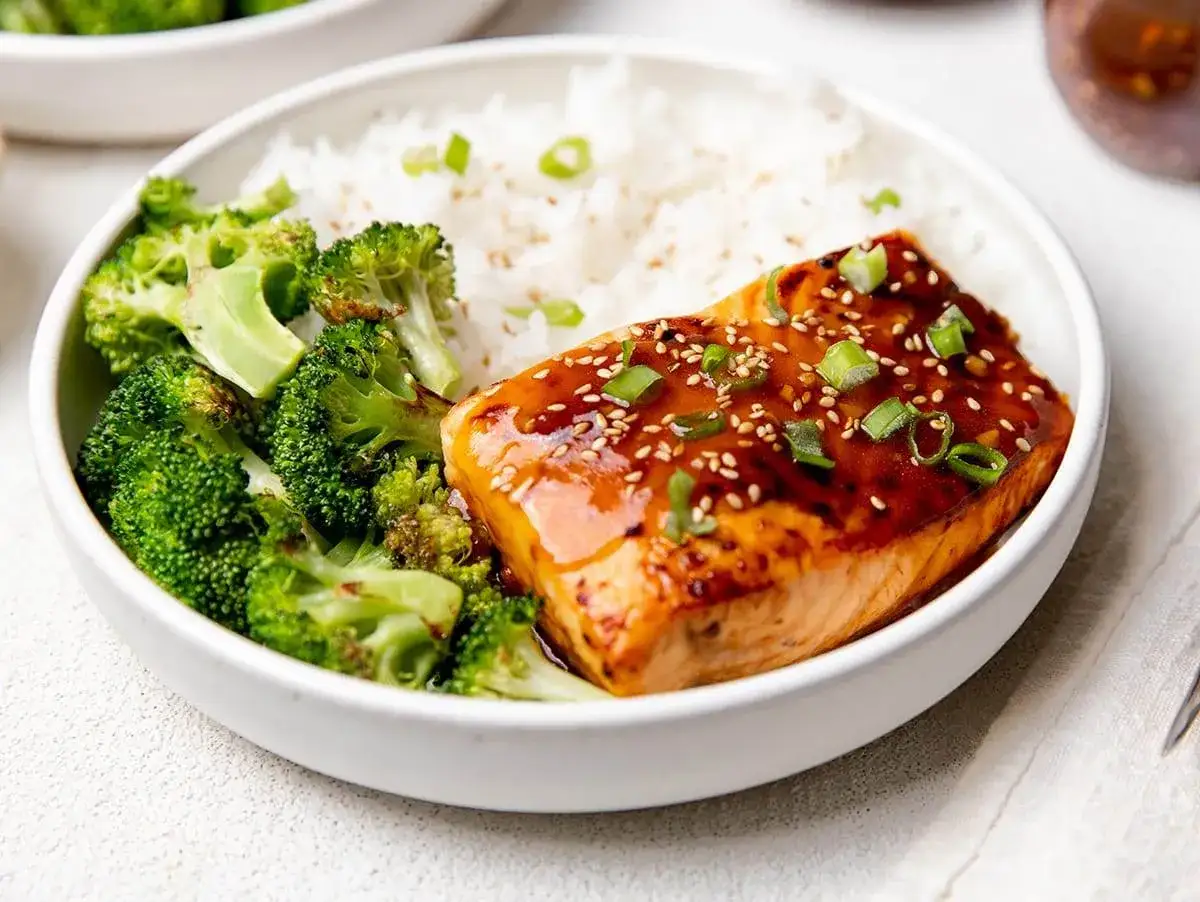 En skål med ris, ångad broccoli och en glaserad asiatisk laxfilé toppad med sesamfrön och salladslök.