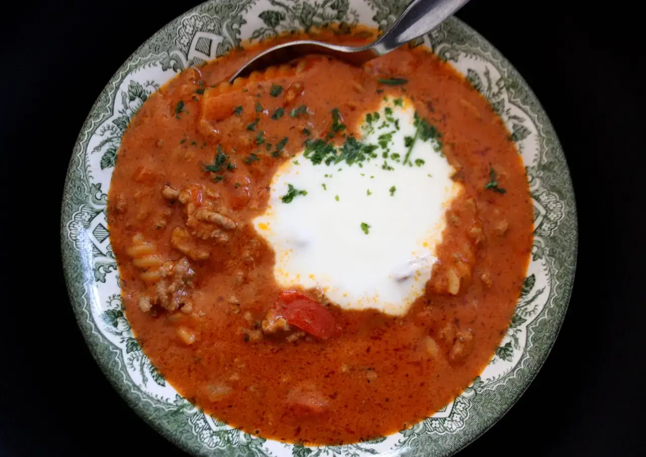 En skål med köttfärssoppa med pasta, toppad med en klick gräddfil och persilja. Perfekt för barn som älskar en värmande måltid.