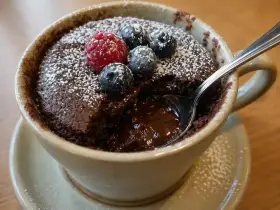En kladdkaka i micro, toppad med bär och pudrat socker. En sked är nedsatt i den rinnande chokladen.