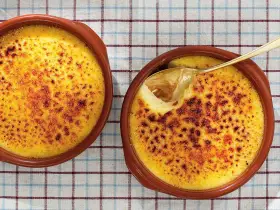 Två krämiga creme brulee i bruna skålar, en med en gyllene sked som lyfter fram den karamelliserade ytan.