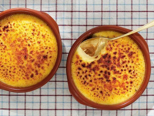 Två krämiga creme brulee i bruna skålar, en med en gyllene sked som lyfter fram den karamelliserade ytan.