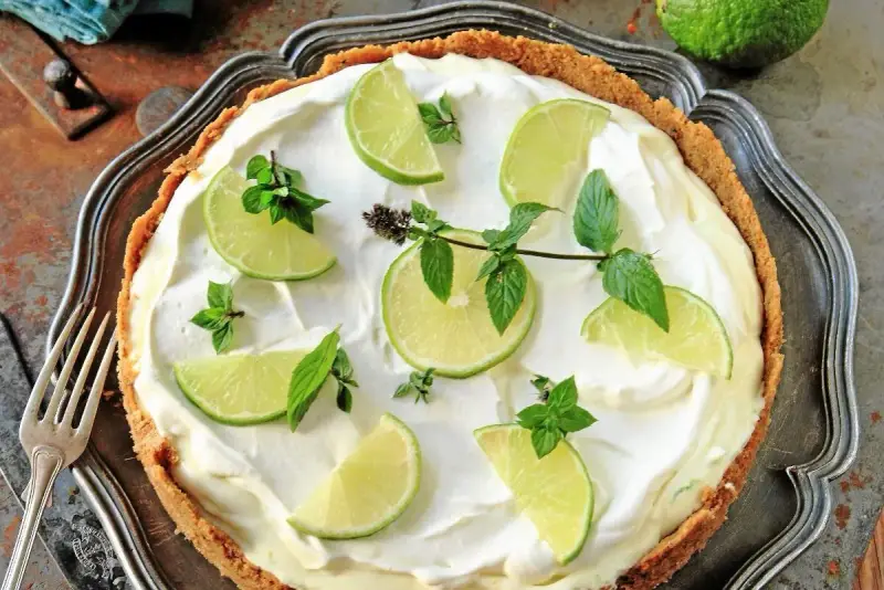 En krämig key lime pie med limeklyftor och mynta på en krispig botten, serverad på ett vackert fat.