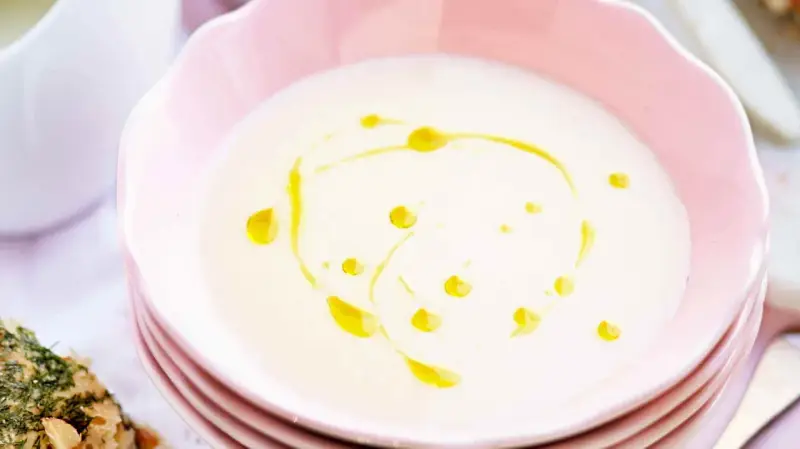 En krämig vit sparrissoppa med en virvel av olivolja i en rosa skål. Serveras med ett kryddigt bröd.