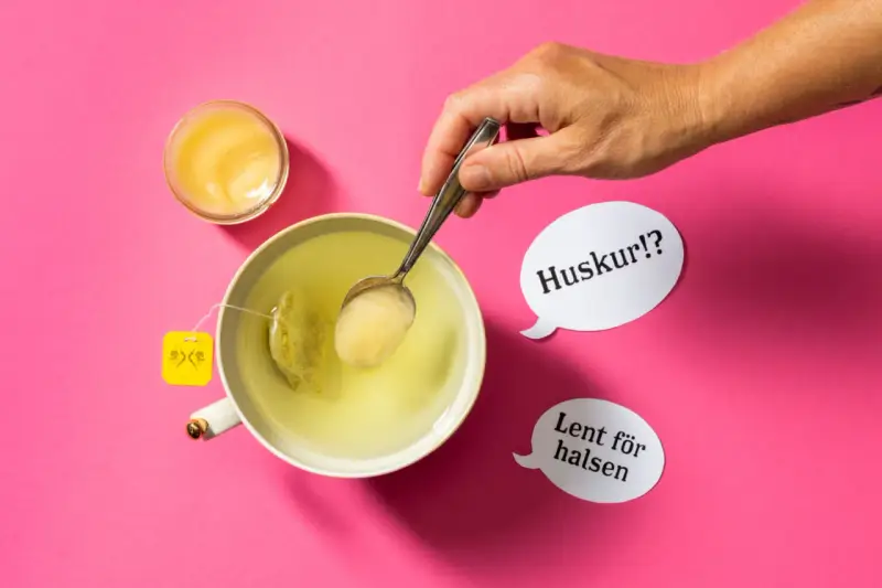 En hand lägger honung i en kopp te. Honung nyttigt för halsen, viskar pratbubblorna.